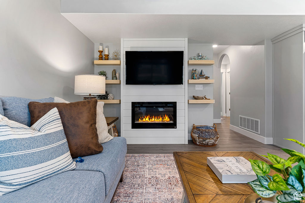 Living room with a fireplace, arched walkways, wood finished floors, and baseboards