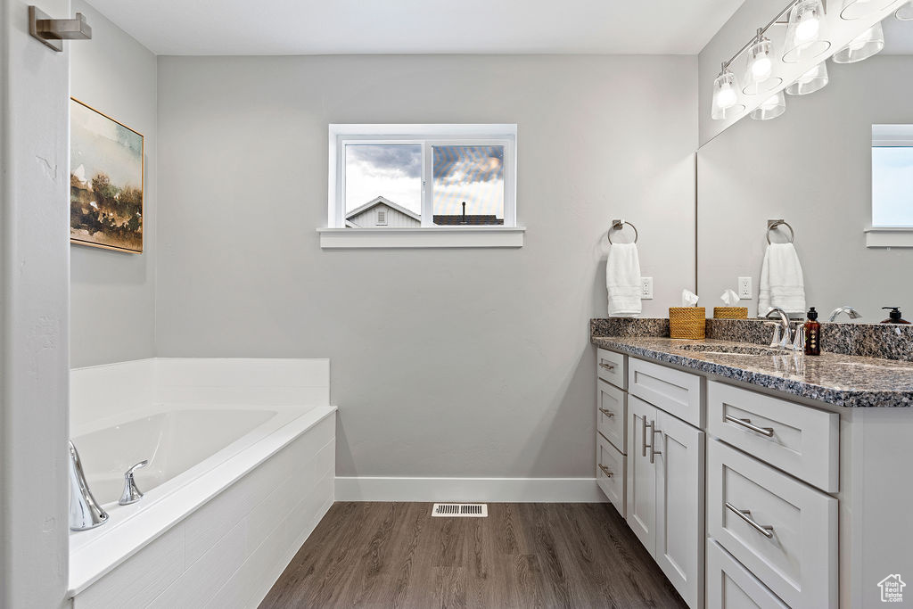 Full bath with wood finished floors, vanity, a garden tub, and baseboards