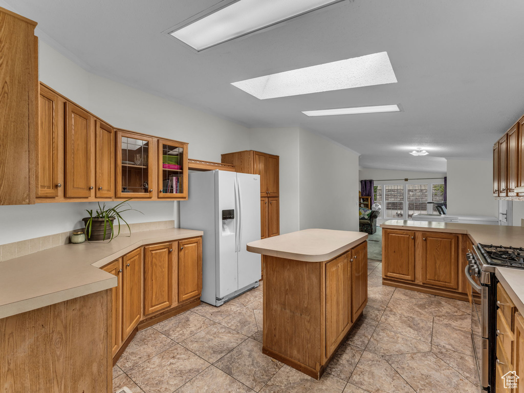 Kitchen featuring white fridge with ice dispenser, gas range, a skylight, a center island, and glass insert cabinets