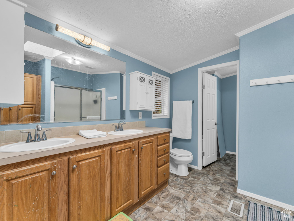 Bathroom with a shower stall, a textured ceiling, double vanity, toilet, and baseboards