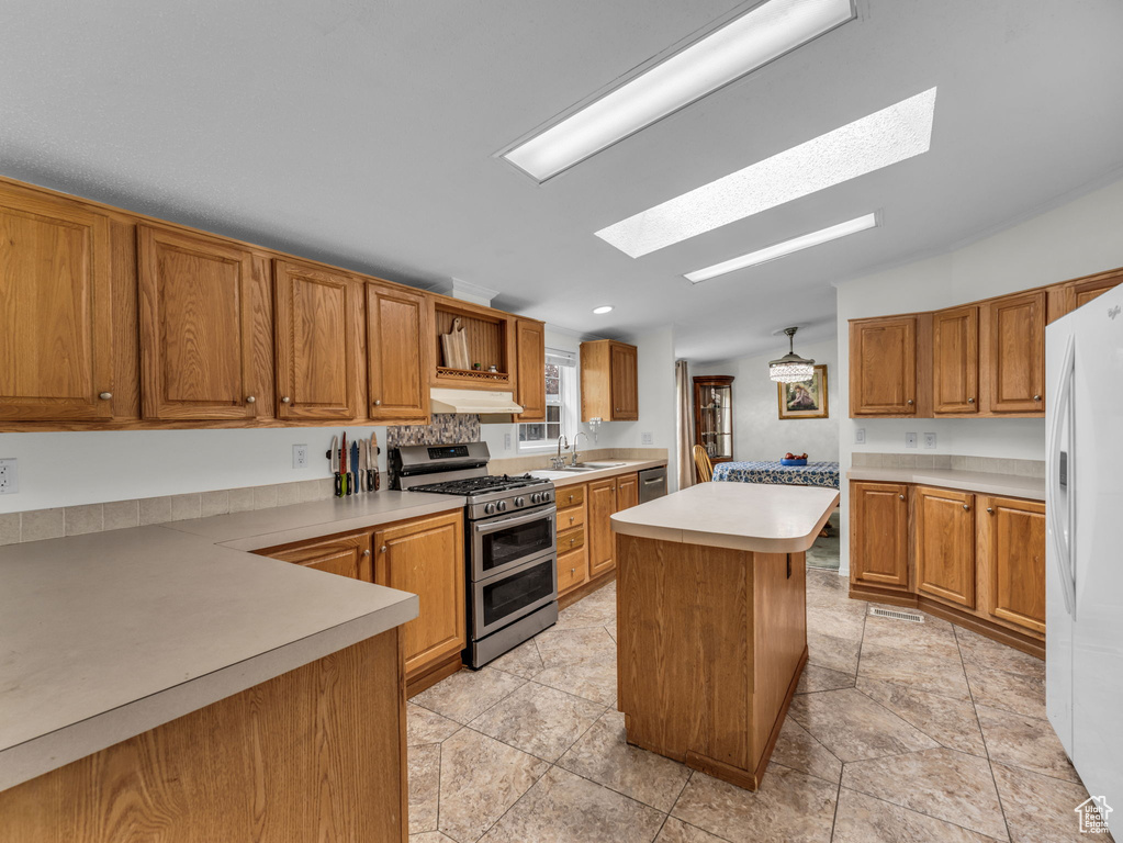 Kitchen with appliances with stainless steel finishes, a skylight, a sink, light countertops, and a kitchen island