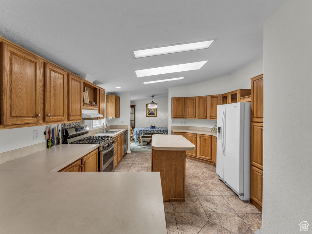 Kitchen with stainless steel appliances, a skylight, a sink, under cabinet range hood, and light countertops