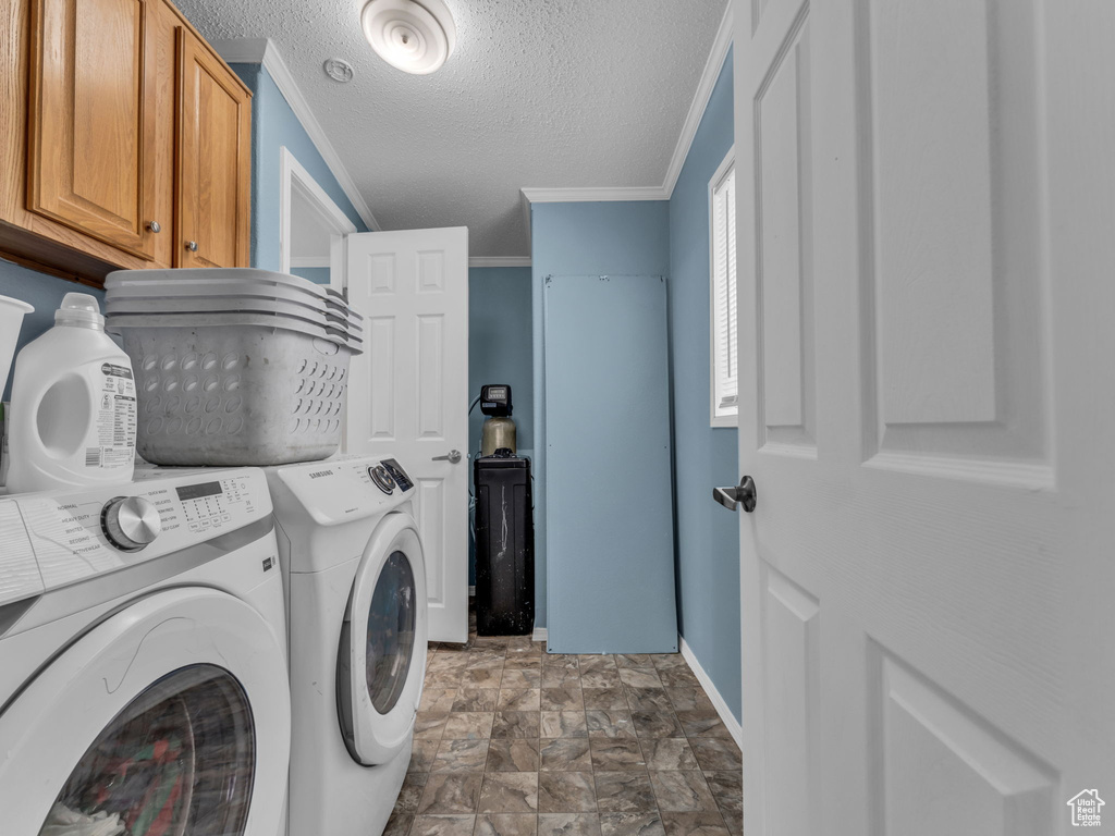 Clothes washing area with cabinet space, ornamental molding, washing machine and clothes dryer, baseboards, and a textured ceiling