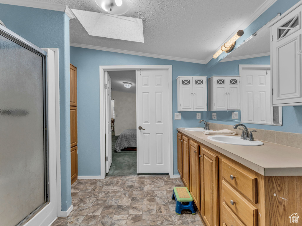 Bathroom featuring a shower stall, baseboards, double vanity, a textured ceiling, and vaulted ceiling