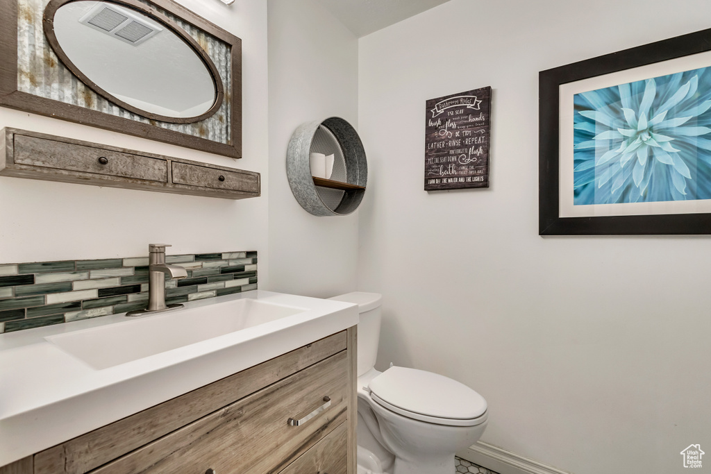 Half bath featuring toilet, vanity, visible vents, decorative backsplash, and baseboards