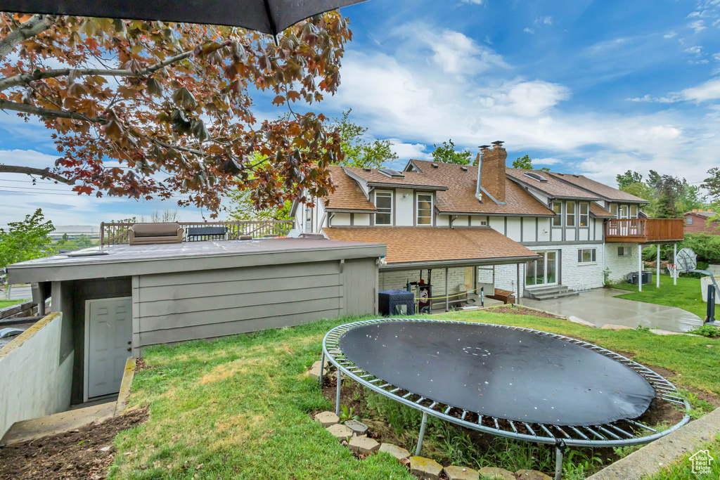 Rear view of house featuring roof with shingles, a trampoline, brick siding, a patio, and a lawn