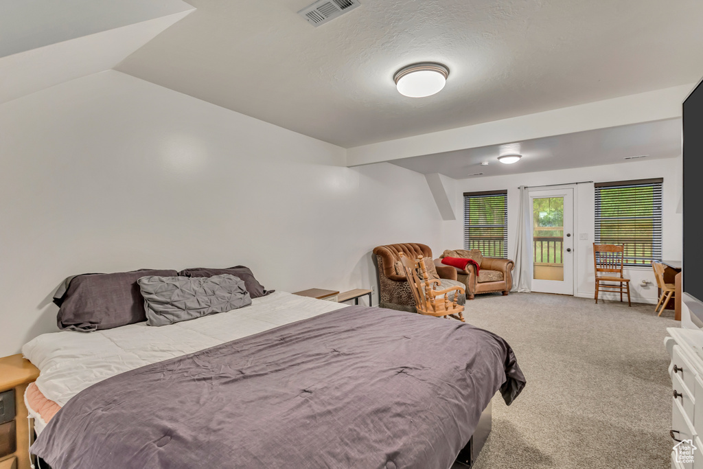 Carpeted bedroom featuring vaulted ceiling, visible vents, and access to exterior