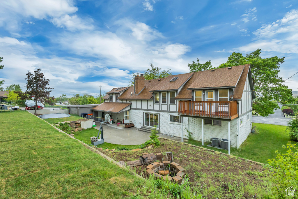 Back of house featuring a patio, a fire pit, a wooden deck, a lawn, and roof with shingles