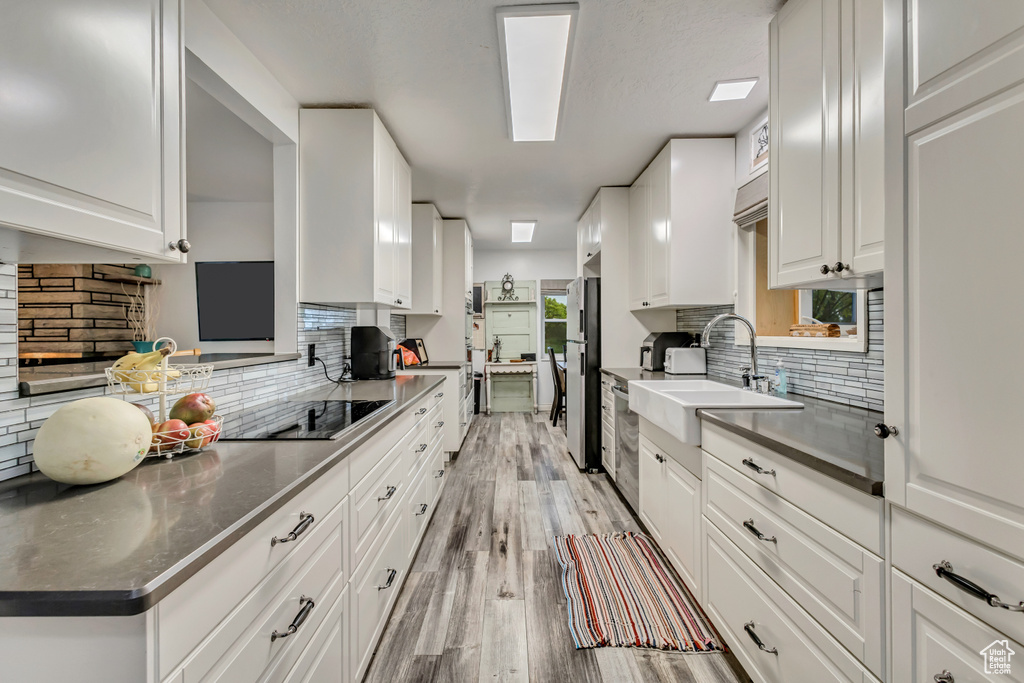 Kitchen with a sink, stainless steel appliances, light wood-type flooring, backsplash, and white cabinets
