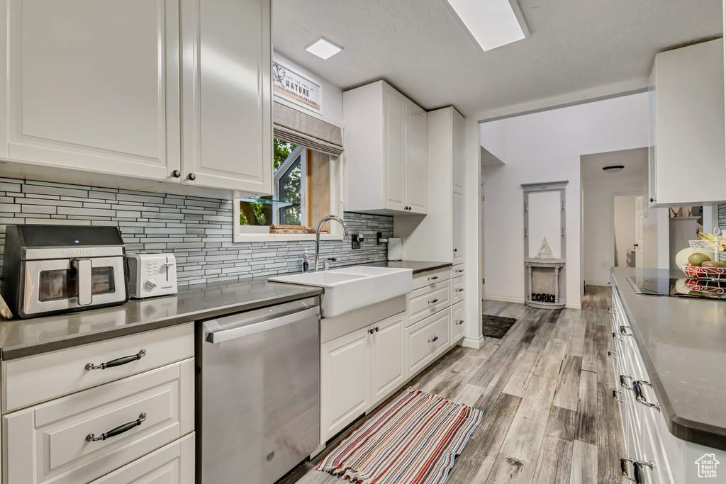 Kitchen with a sink, dishwasher, light wood-style flooring, decorative backsplash, and black electric cooktop