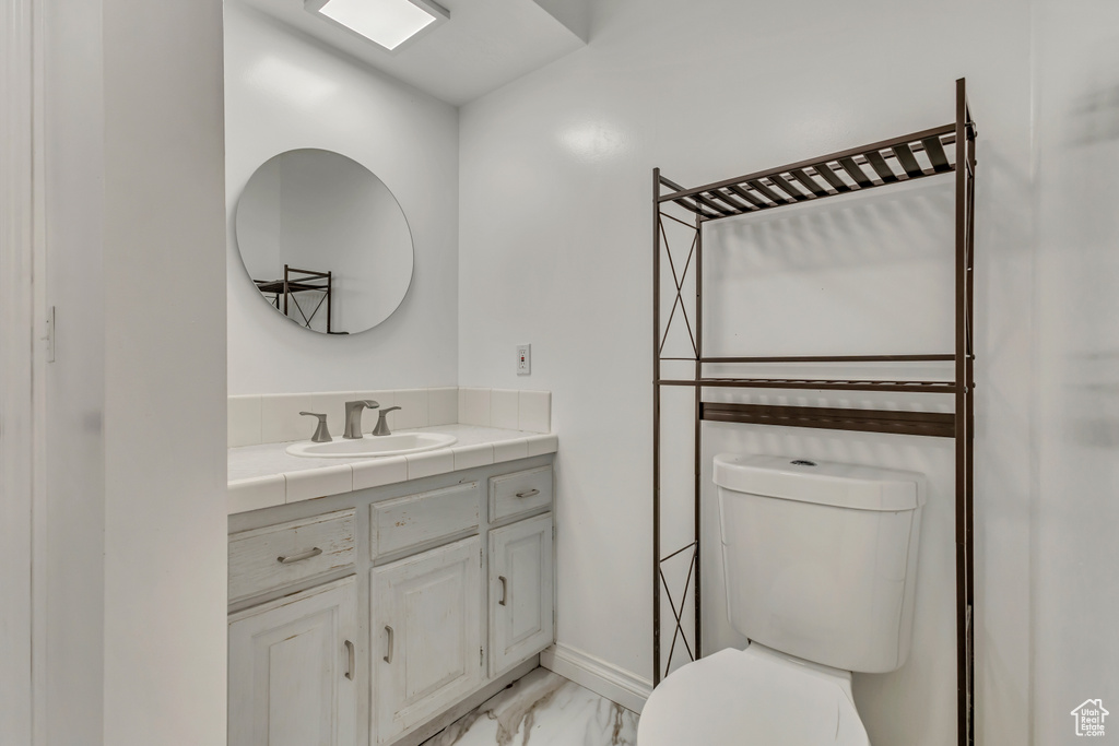 Bathroom featuring toilet, baseboards, marble finish floor, and vanity