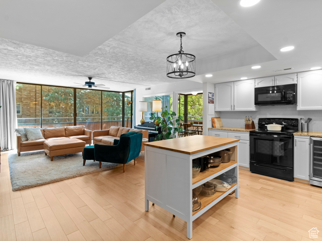 Kitchen with black appliances, light wood-style flooring, white cabinets, wine cooler, and open shelves