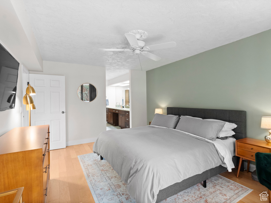 Bedroom with light wood-style floors, ceiling fan, ensuite bath, and baseboards