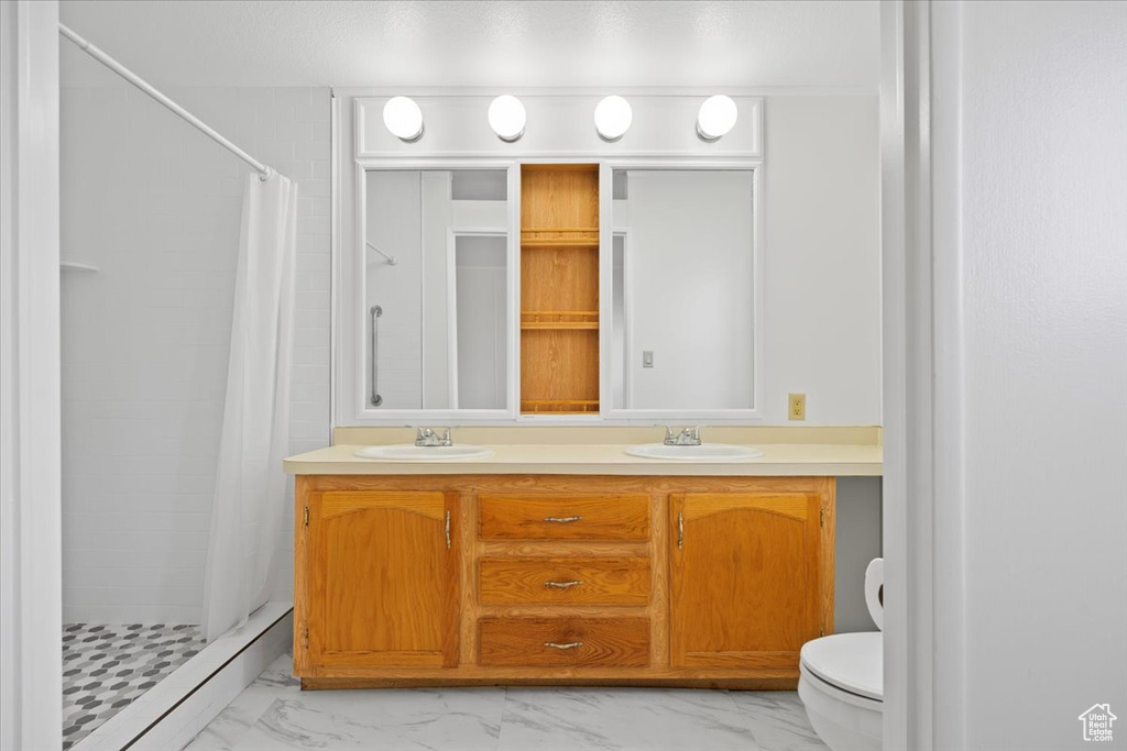 Bathroom featuring toilet, marble finish flooring, a stall shower, and double vanity