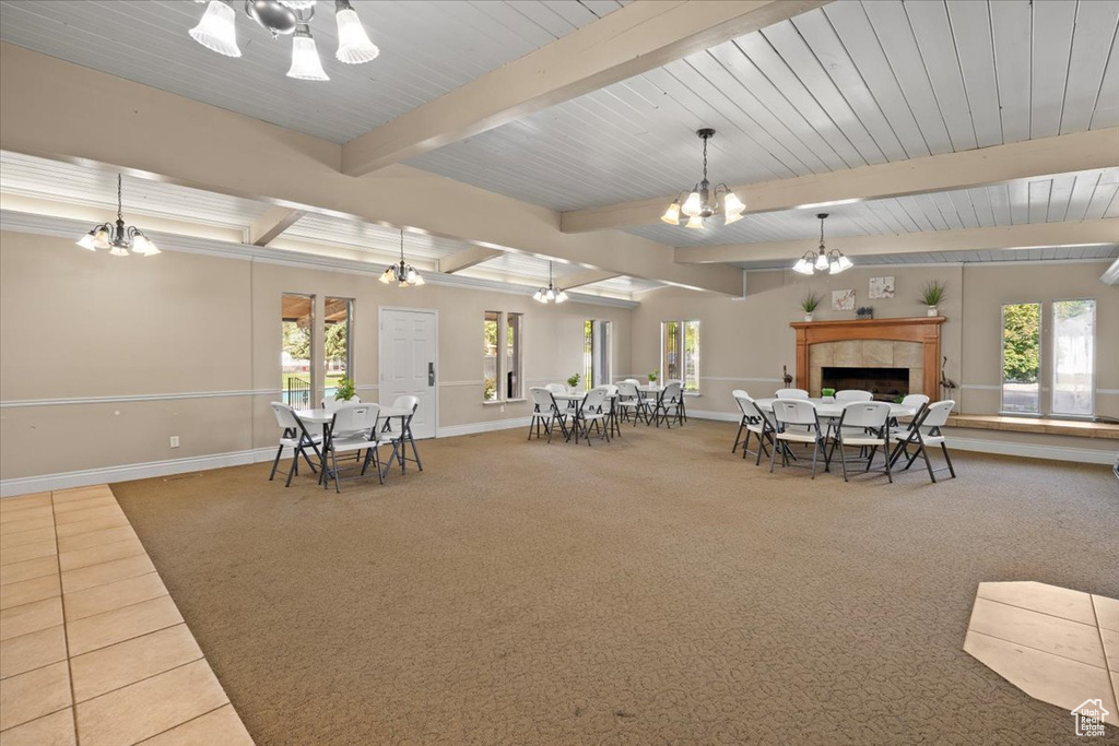 Carpeted dining room featuring a chandelier, baseboards, beamed ceiling, and a tile fireplace
