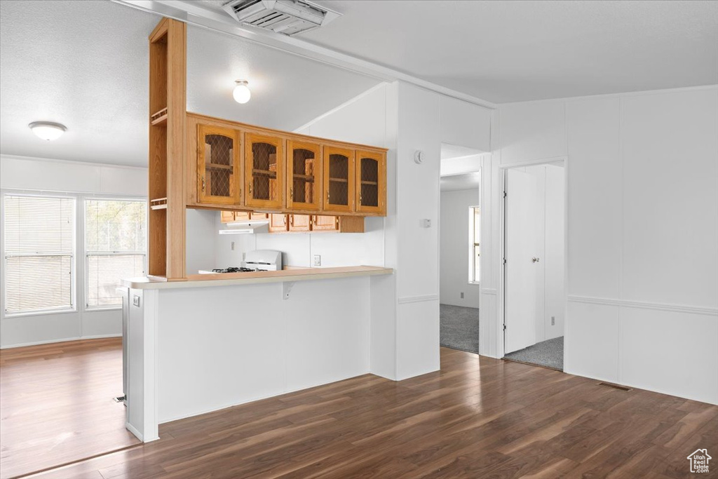 Kitchen featuring wood finished floors, glass insert cabinets, brown cabinets, a kitchen bar, and light countertops