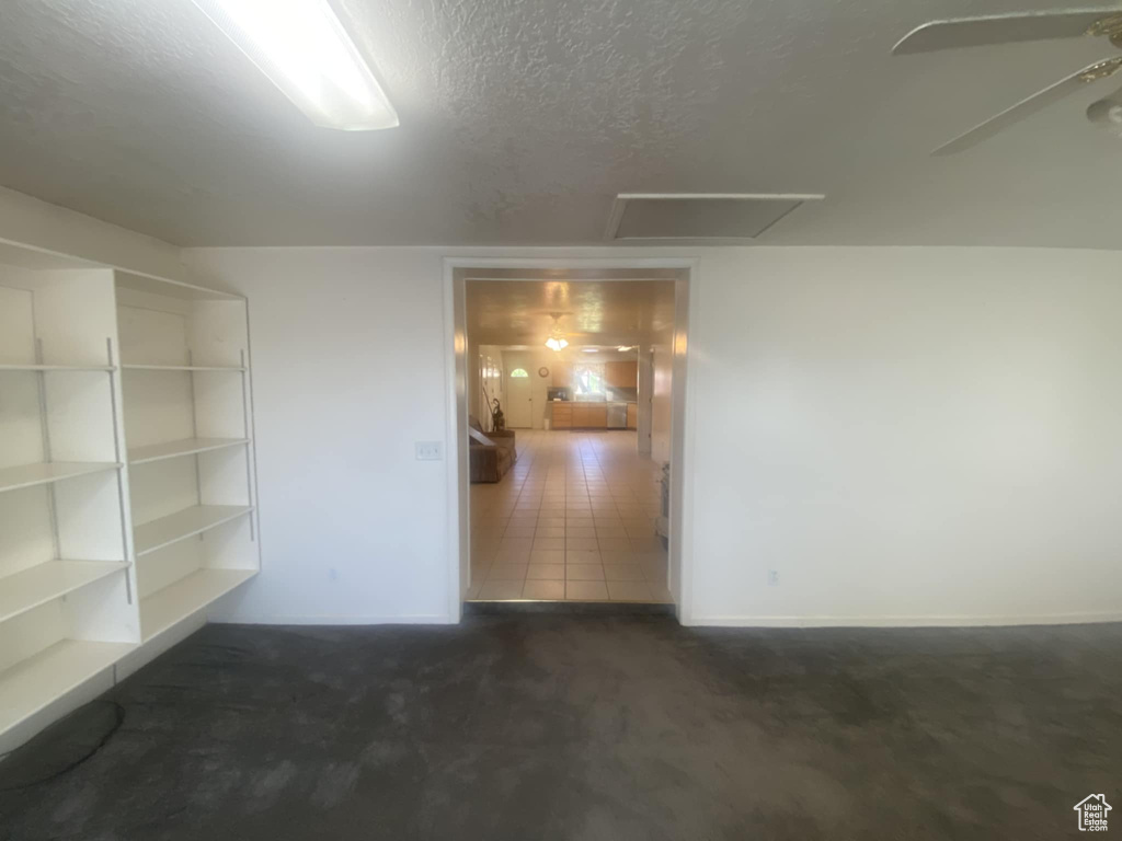 Unfurnished room featuring a textured ceiling, ceiling fan, dark colored carpet, and attic access