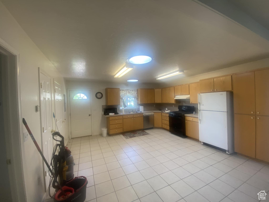 Kitchen with freestanding refrigerator, black gas range oven, under cabinet range hood, dishwasher, and light countertops