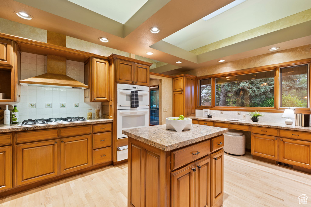 Kitchen featuring wall chimney range hood, light wood-type flooring, and brown cabinetry