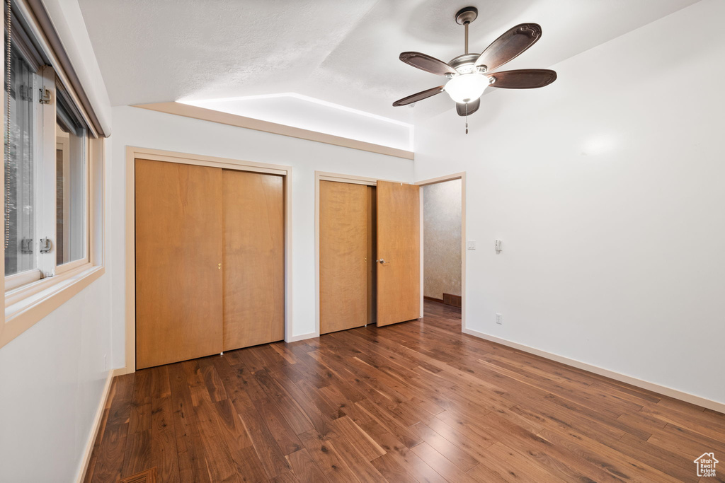 Unfurnished bedroom featuring wood finished floors, multiple closets, baseboards, ceiling fan, and vaulted ceiling