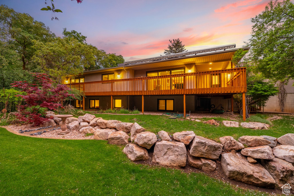 Back of property at dusk with a yard and a deck