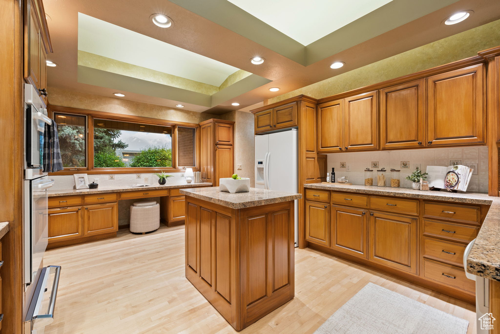 Kitchen featuring brown cabinets, white refrigerator with ice dispenser, light wood-type flooring, and decorative backsplash