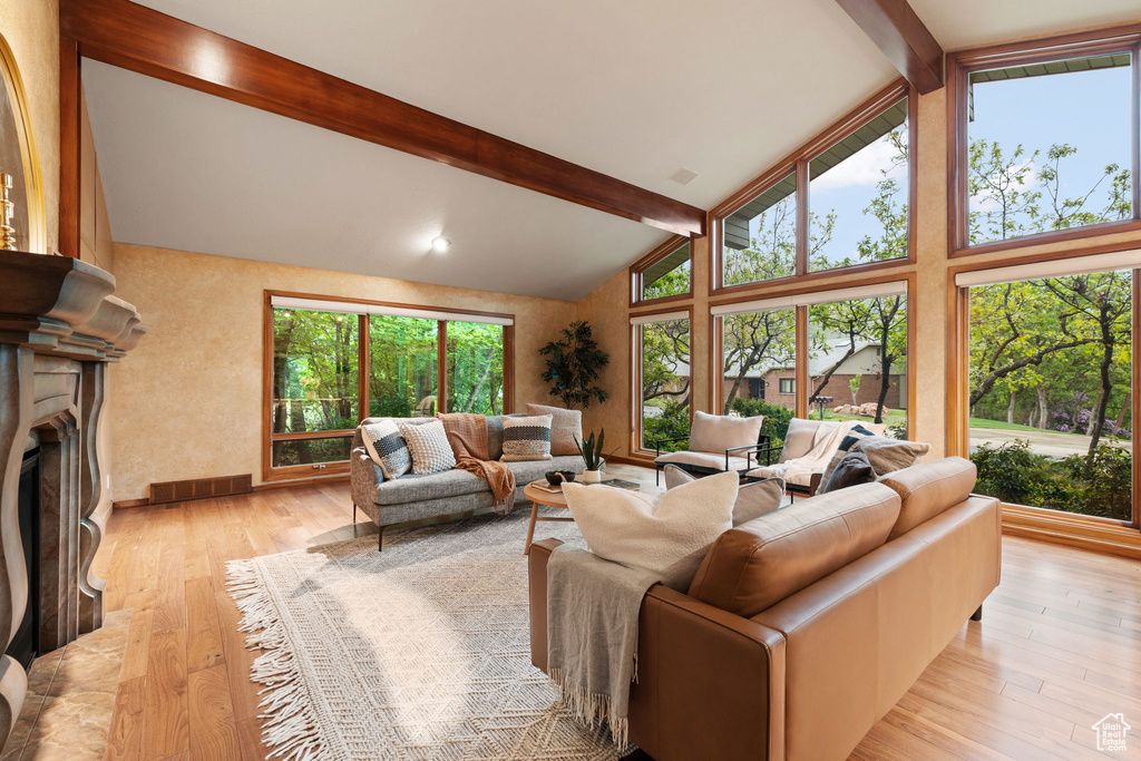 Living room featuring beam ceiling, a fireplace, light wood finished floors, and high vaulted ceiling