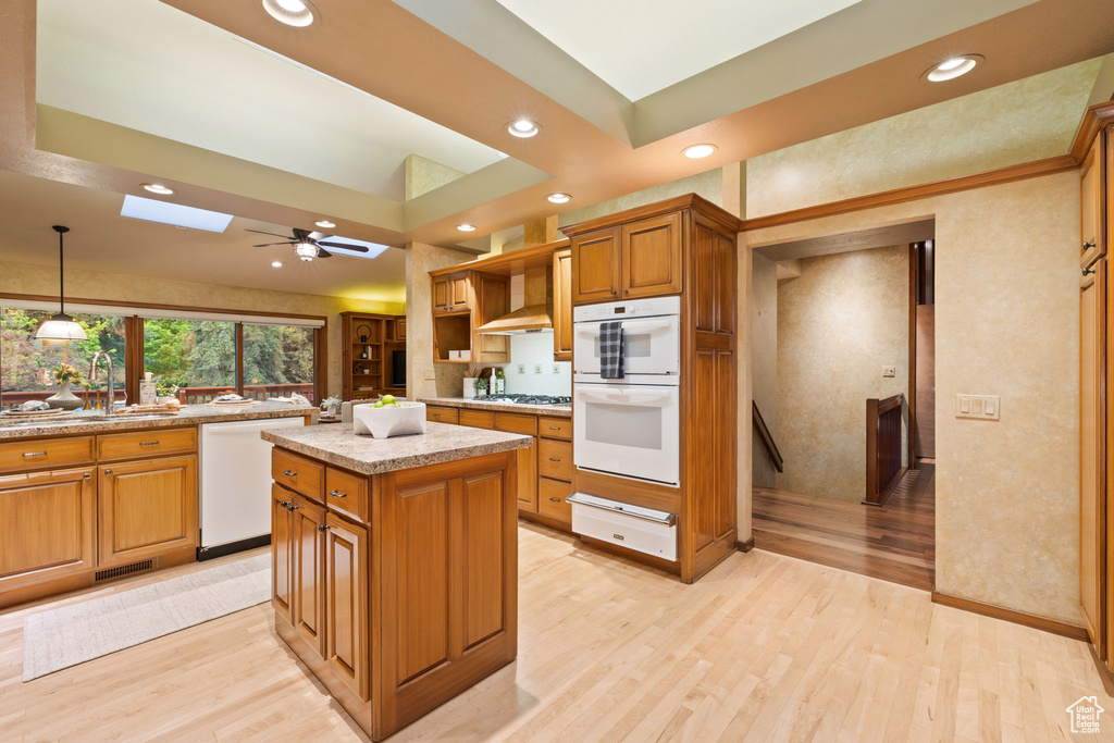 Kitchen featuring a warming drawer, white appliances, light wood-type flooring, and a skylight
