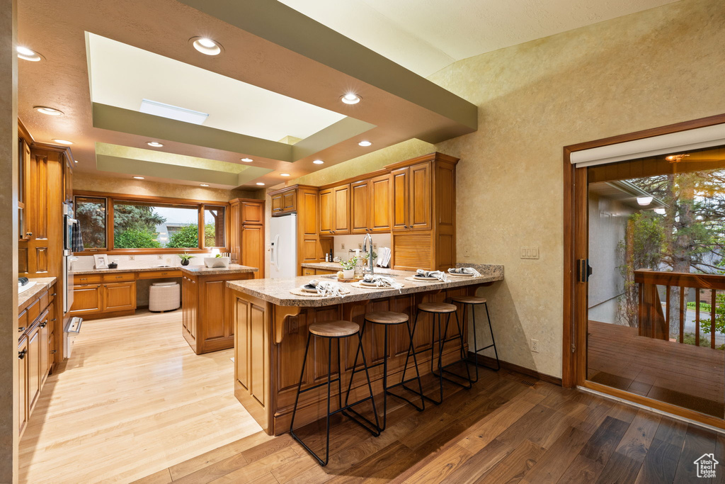 Kitchen with a peninsula, brown cabinets, a kitchen breakfast bar, light wood-type flooring, and white fridge with ice dispenser