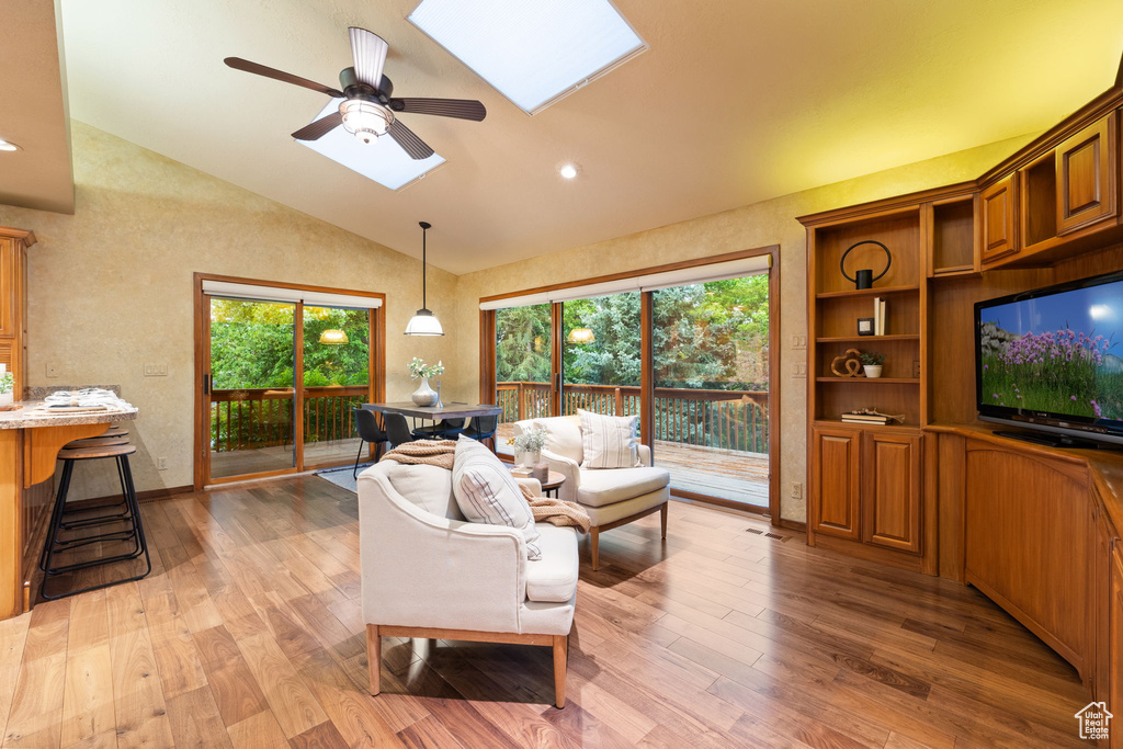 Living room featuring a ceiling fan, light wood-style floors, a skylight, and a healthy amount of sunlight