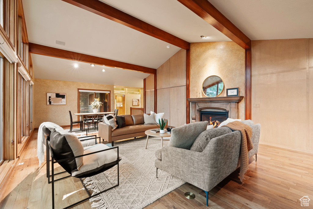 Living room with a lit fireplace, lofted ceiling with beams, and hardwood / wood-style flooring