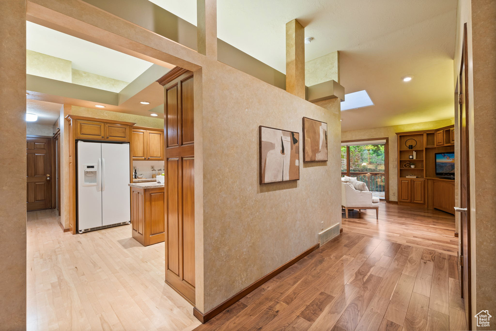 Hallway with baseboards, recessed lighting, light wood-type flooring, and a skylight