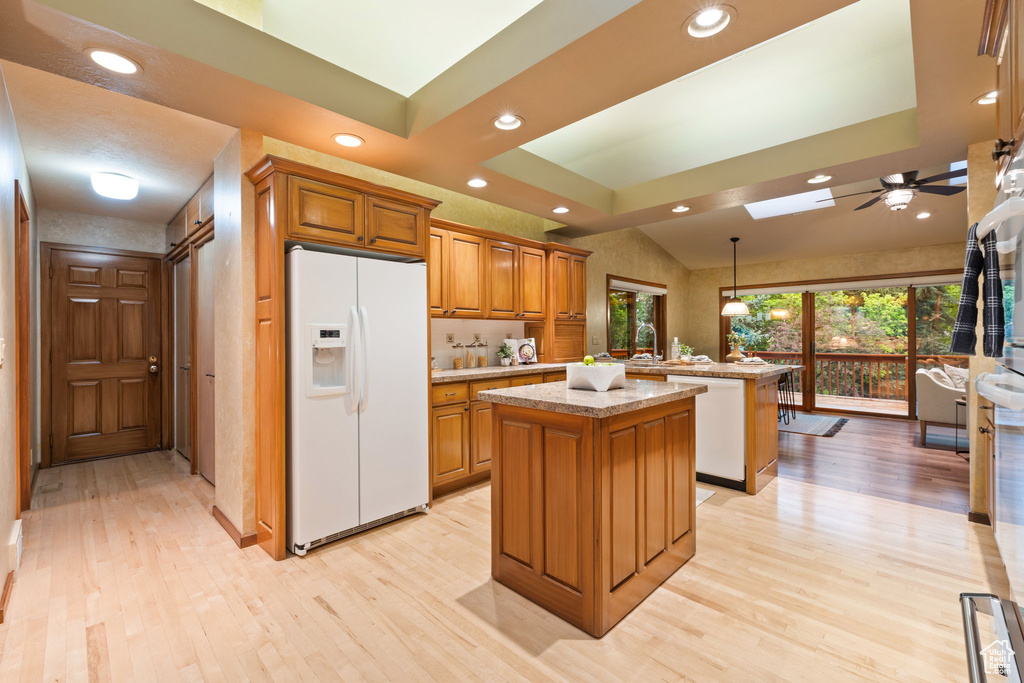 Kitchen featuring a skylight, white appliances, brown cabinets, light wood-type flooring, and a kitchen island