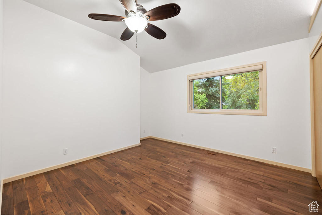 Empty room featuring ceiling fan, vaulted ceiling, baseboards, and wood-type flooring