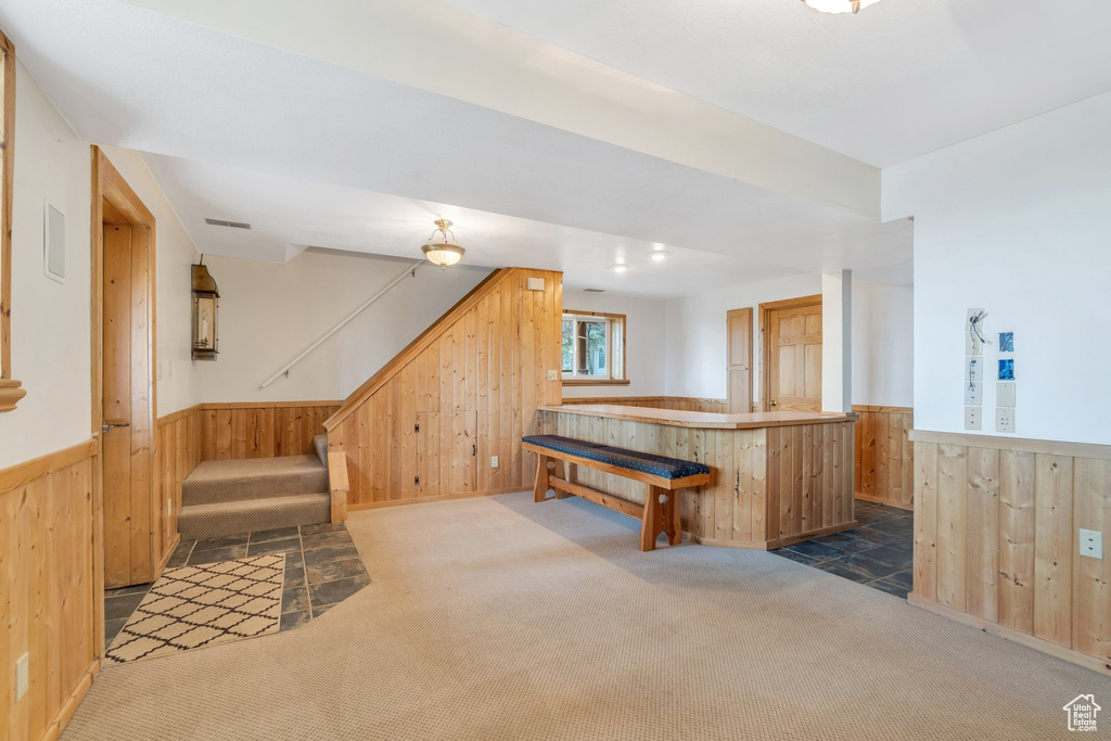 Bar featuring wooden walls, a wainscoted wall, carpet flooring, and stairs