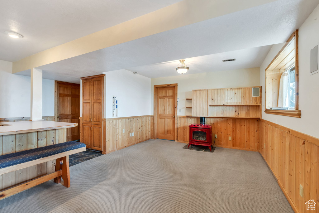 Unfurnished room with wainscoting, wood walls, a wood stove, and light carpet