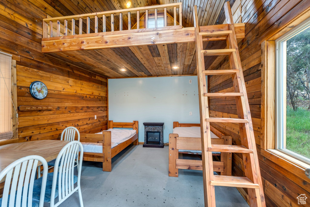 Bedroom with concrete floors, wooden walls, multiple windows, and wooden ceiling