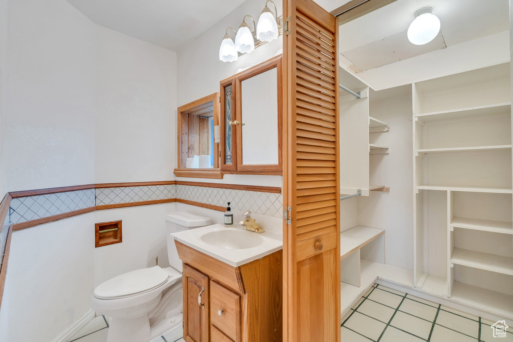 Bathroom featuring tile patterned flooring, toilet, vanity, and a wainscoted wall