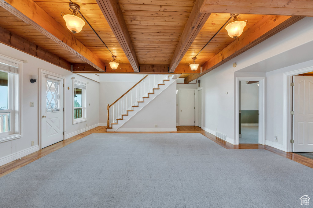 Unfurnished living room featuring wood ceiling, stairs, baseboards, light colored carpet, and beamed ceiling