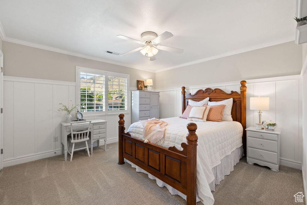 Bedroom with light carpet, a decorative wall, ornamental molding, and ceiling fan