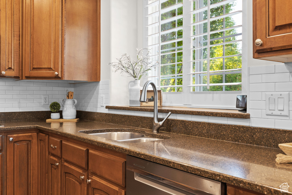 Kitchen featuring dishwasher, a sink, backsplash, brown cabinetry, and dark stone counters