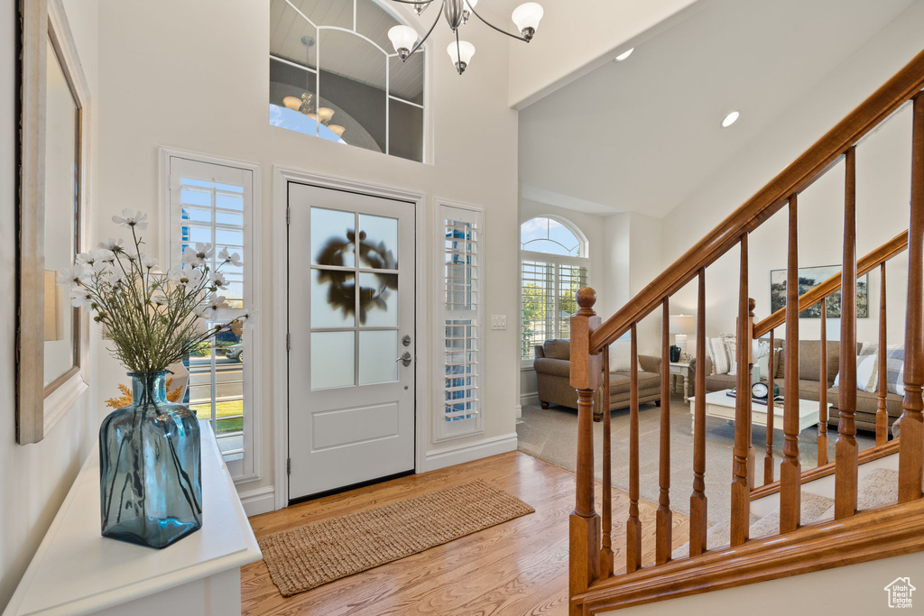 Foyer with a towering ceiling, wood finished floors, a chandelier, stairs, and recessed lighting