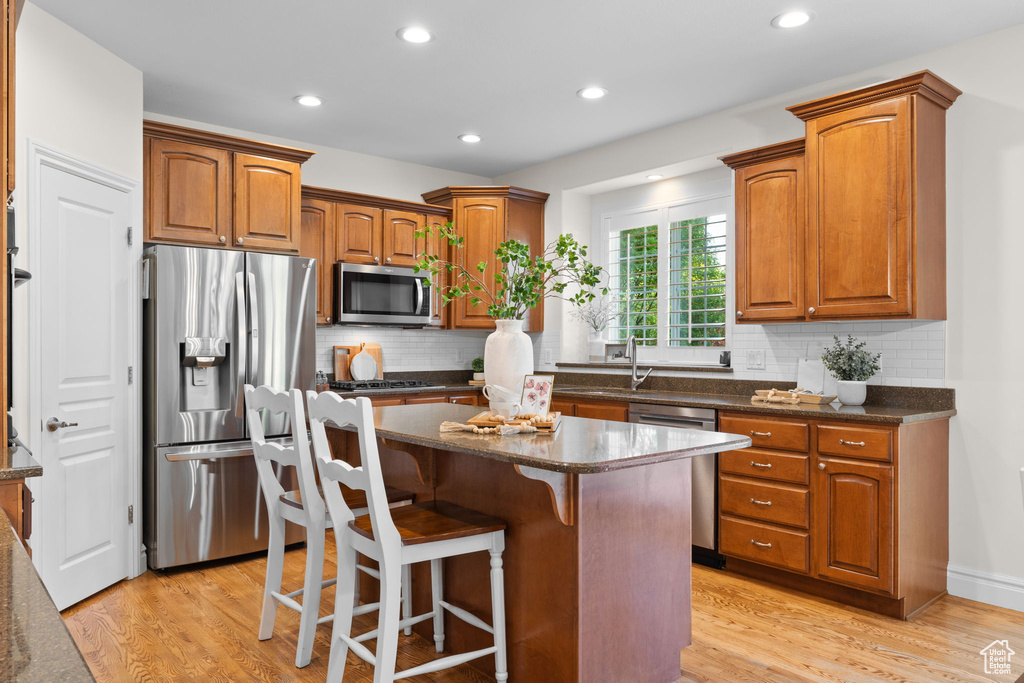 Kitchen with appliances with stainless steel finishes, a kitchen island, light wood finished floors, brown cabinetry, and recessed lighting