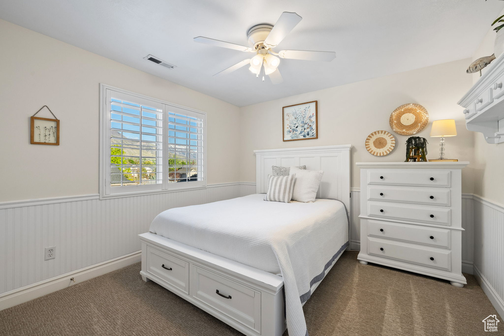 Bedroom with wainscoting, dark carpet, and a ceiling fan
