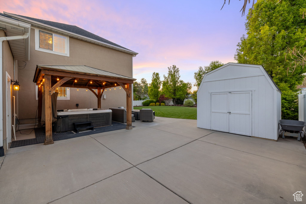Patio terrace at dusk featuring a hot tub, a gazebo, a shed, a lawn, and cooling unit