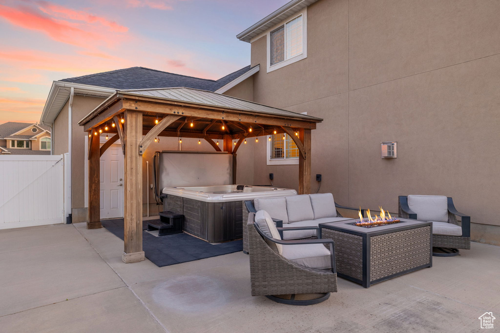 Patio terrace at dusk with a gazebo, a hot tub, fence, and an outdoor living space with a fire pit