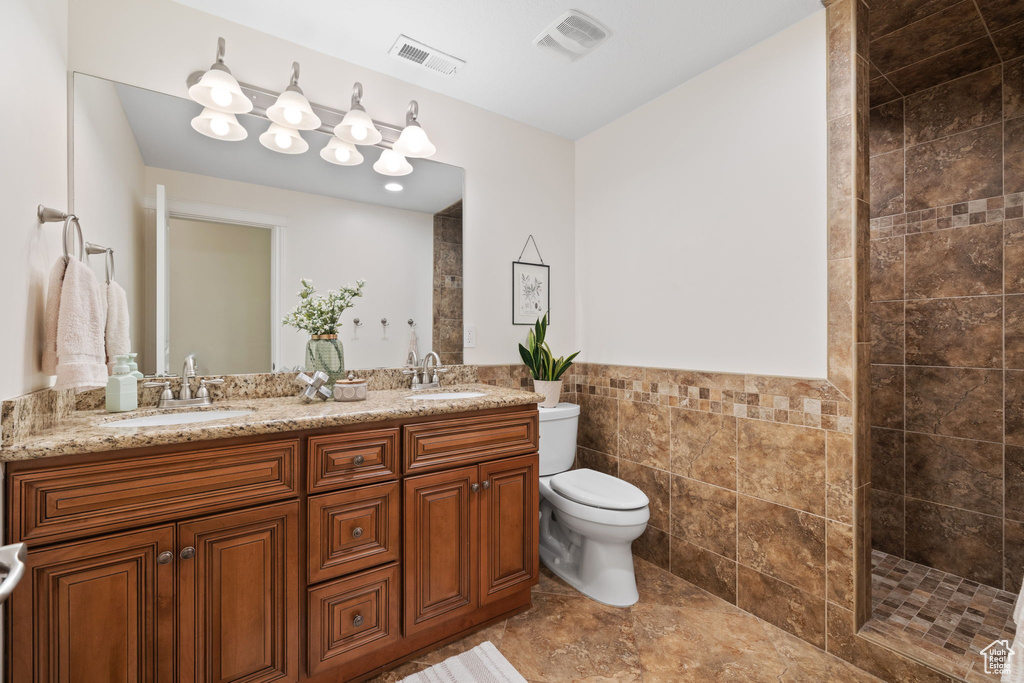 Bathroom with toilet, tile walls, walk in shower, double vanity, and a wainscoted wall