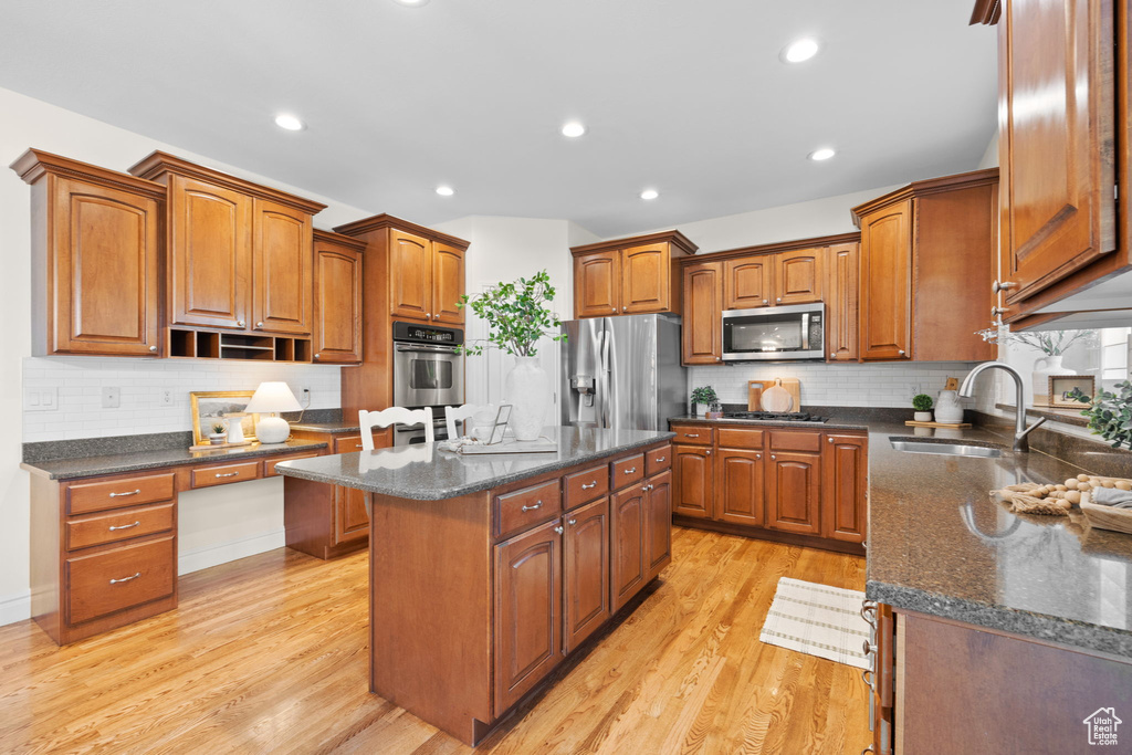 Kitchen with a sink, stainless steel appliances, light wood-style floors, a kitchen island, and brown cabinets