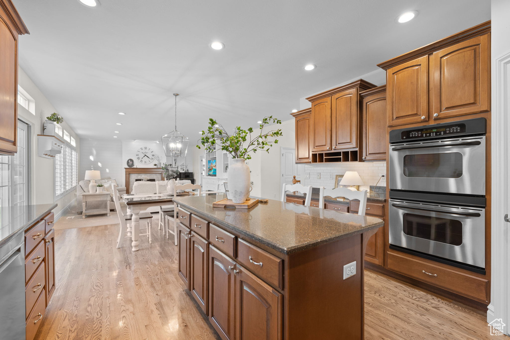 Kitchen featuring appliances with stainless steel finishes, a kitchen island, light wood-type flooring, decorative backsplash, and recessed lighting