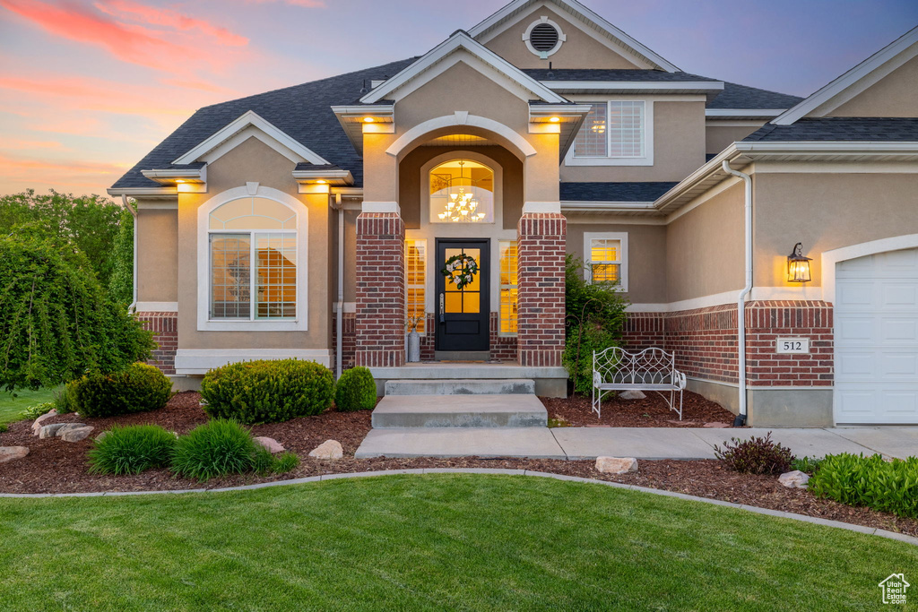 Entrance to property featuring stucco siding, a lawn, brick siding, and roof with shingles